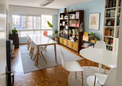 Sala polivalente en lapiz desarrollo para talleres y terapia grupal con mesas blancas, sillas modernas y estanterías llenas de material didáctico