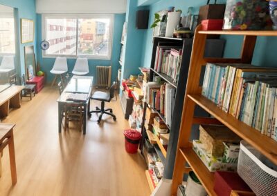 Sala polivalente en lapiz desarrollo para talleres y terapia grupal con mesas blancas, sillas modernas y estanterías llenas de material didáctico